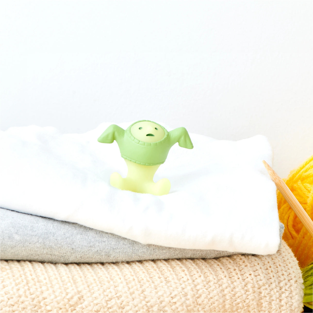 A small, green silicone stopper in the shape of a character from the Smiski Dressing Series - Blind Box by Smiski sits on a stack of folded towels.