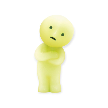 A small, glowing, green figurine with a round head, black eyes, and mouth stands with folded arms, gazing upwards. This intriguing character is from the Smiski At Work Series by Smiski and comes in a blind box for an exciting surprise.