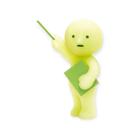 A Smiski At Work Series figure by Smiski features a yellow stick figure holding a green square and pointing with a stick, poised for action. An unexpected twist adds intrigue to this charming scene: it glows in the dark.