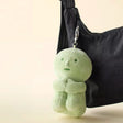 Light green plush doll keychain with small limbs hanging from black fabric bag strap