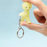 A person holds the Smiski Keychain - Carrying Key Figure, a delightful small yellow figurine from Smiski, featuring a metal chain and round keyring. This charming accessory not only serves practical purposes for carrying keys but also glows in the dark, adding a touch of magic to everyday essentials.