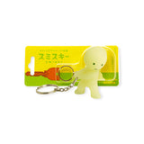 The delightful Smiski Keychain - Carrying Key Figure, presented by the Smiski brand, is encased in a clear package set against a lively yellow and green background, ideal for infusing your key collection with whimsical charm.