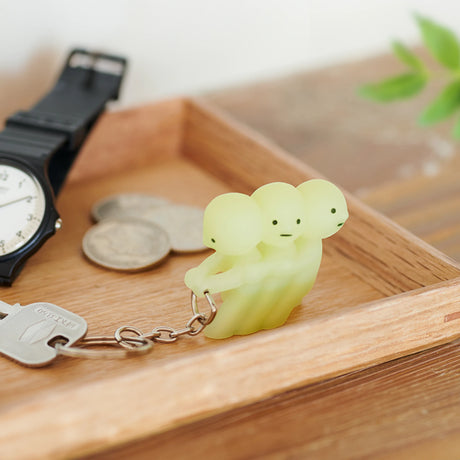 A Smiski Pulling Key Figure keychain from Smiski with three heads is placed in a wooden tray along with coins and a black watch, ensuring you never lose your keys.