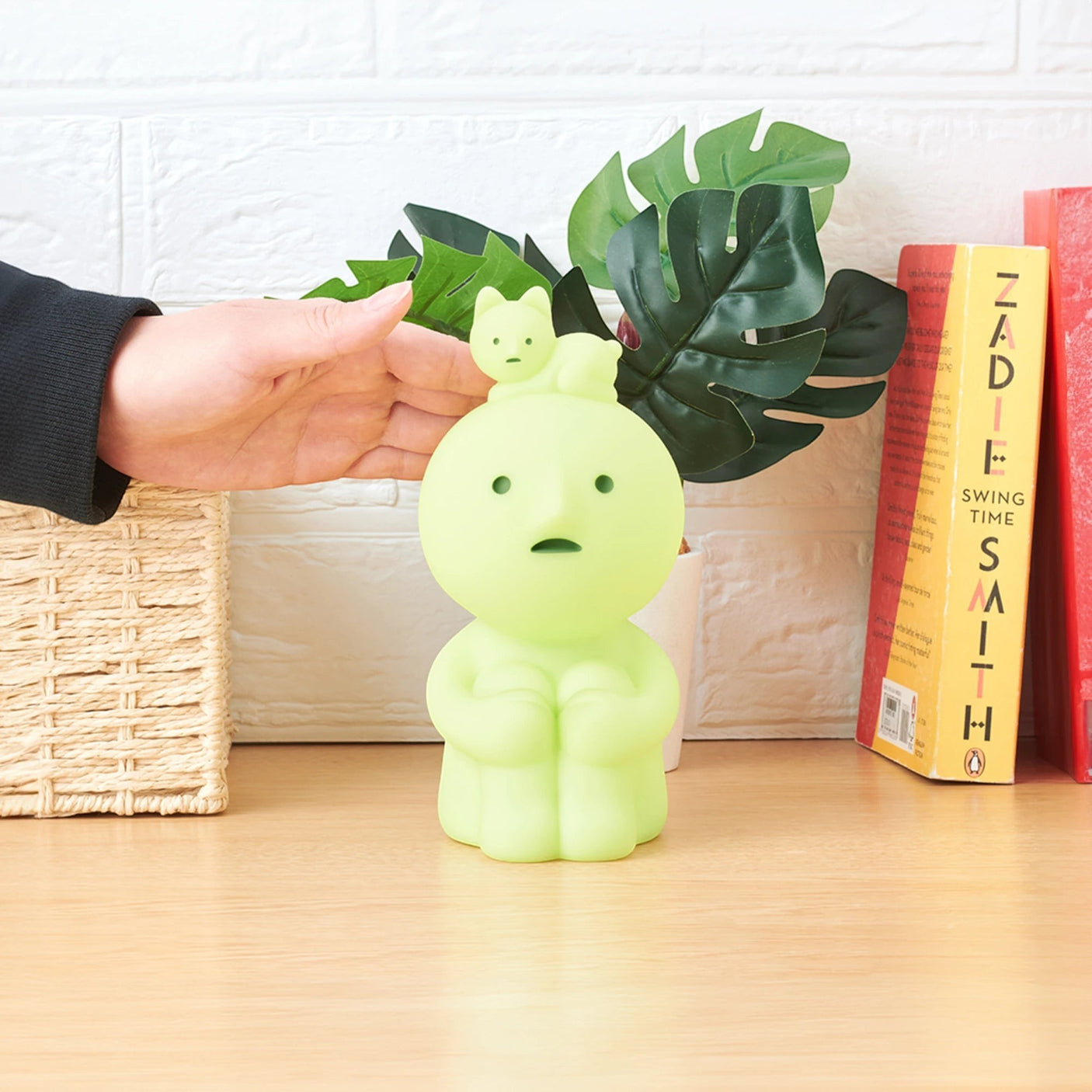 Mint-green Smiski touch light figure hugging knees, being placed by a hand