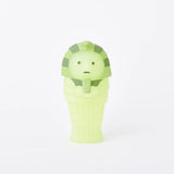 A small, lime-green figure shaped like an ancient Egyptian mummy stands upright on a plain white background, part of the Smiski Museum Series - Blind Box collection, featuring imaginative glow-in-the-dark figures.