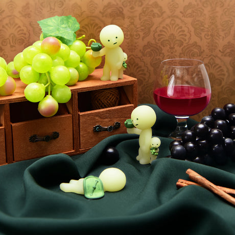 Figurines from the Smiski Museum Series - Blind Box by Smiski are accompanied by a red wine glass and grapes on a green cloth, creating a whimsical and creative setting.