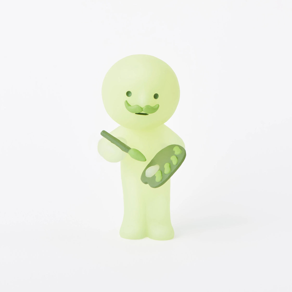 A small figurine from the Smiski Museum Series - Blind Box by Smiski stands holding a paintbrush and palette speckled with green paint spots, smiling against a plain white background. These glow-in-the-dark companions add a creative flair to any space.