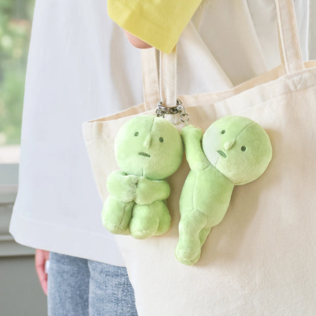 Two Smiski Plush Keychain - Hugging Knees figures by Smiski from Series 1 are attached to a beige tote bag carried by someone in a white shirt and blue jeans, adding a playful touch to the outfit.