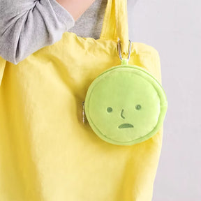 Round lime green plush pouch with simple face design clipped to bright yellow tote bag strap