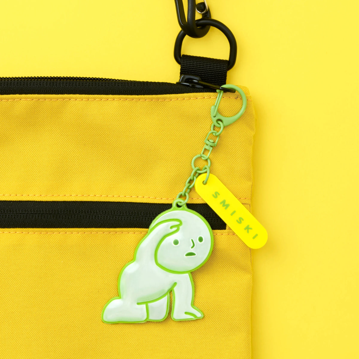 Close-up reflective green Smiski charm on chain attached to yellow pouch