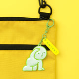 Close-up reflective green Smiski charm on chain attached to yellow pouch