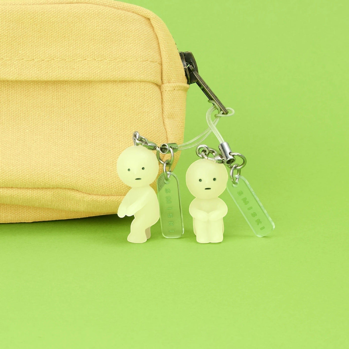 Light green character keychain charms on a beige bag strap with metal hooks