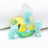 Three small, mint-green figurines with simple facial features are arranged around a box labeled "Smiski Toilet Series - Blind Box" by Smiski. These glow-in-the-dark figures belong to the mini-figures collectibles lineup, with a roll of toilet paper visible in the background.