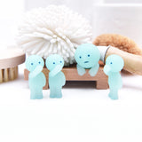 Four Smiski Toilet Series figurines from the Blind Box—three in a standing pose and one leaning against a wooden block—are accompanied by bath brushes and a scrubber. These mini collectibles bring a quirky charm to any bathroom decor.