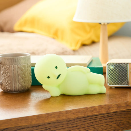 Pale green glowing figurine reclining on wooden table next to textured gray mug and vintage radio speaker