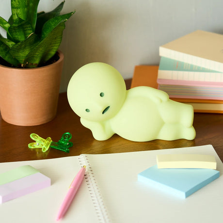 Smiski Touch Light lounging figurine, light-green glow, on desk with stationery