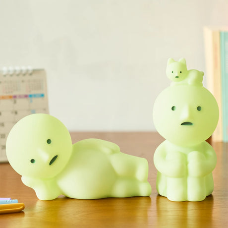 Two pale green character figurines with simple faces on wooden table near calendar and books