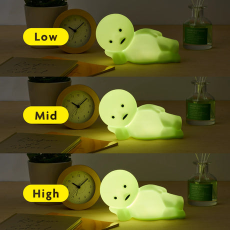 Three images showing increasing brightness levels of a pale green character light on a wooden desk with clock and plants nearby