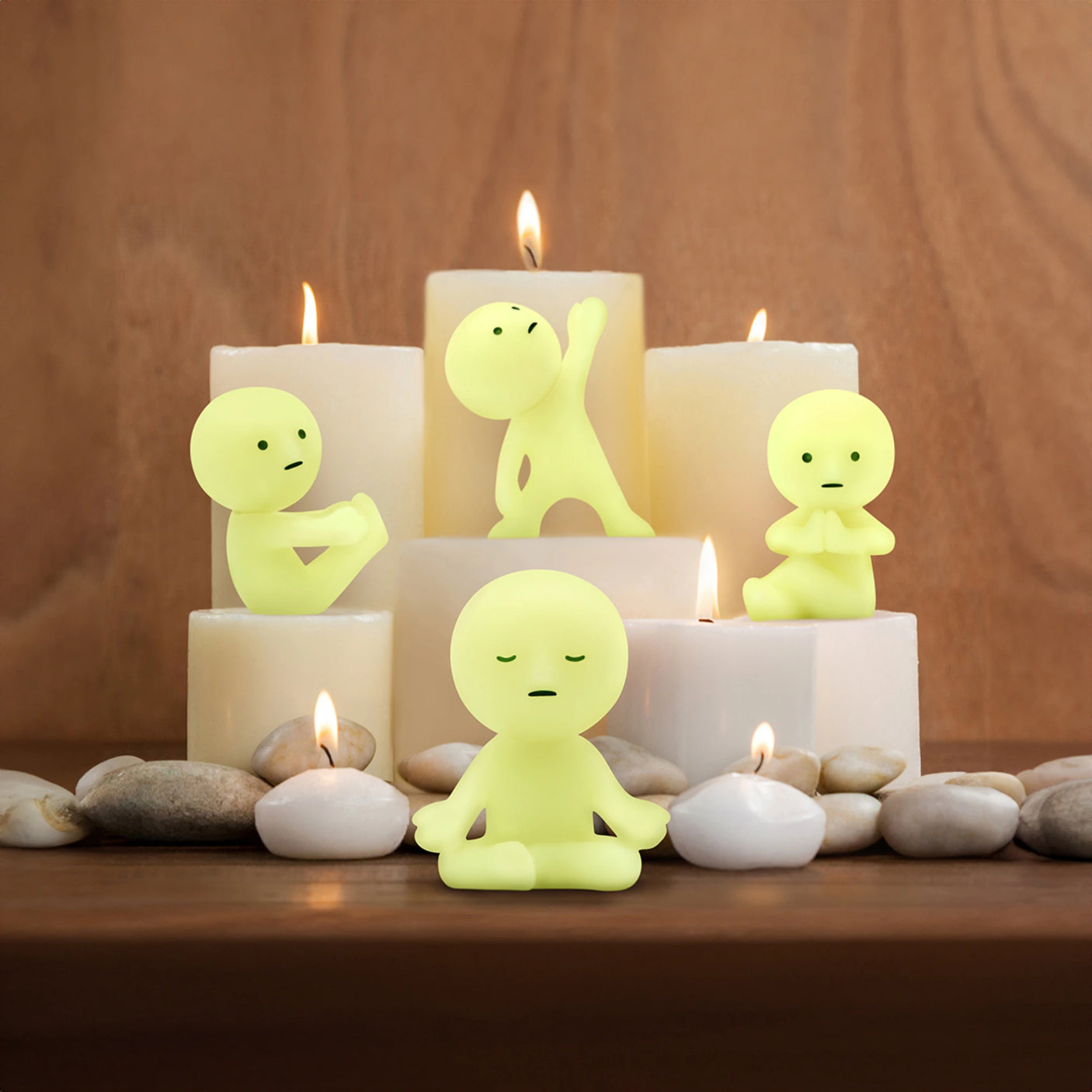 Four Smiski Yoga Series - Blind Box figurines, each from the Smiski brand and striking calming yoga poses, are beautifully arranged around lit candles and stones on a wooden surface.