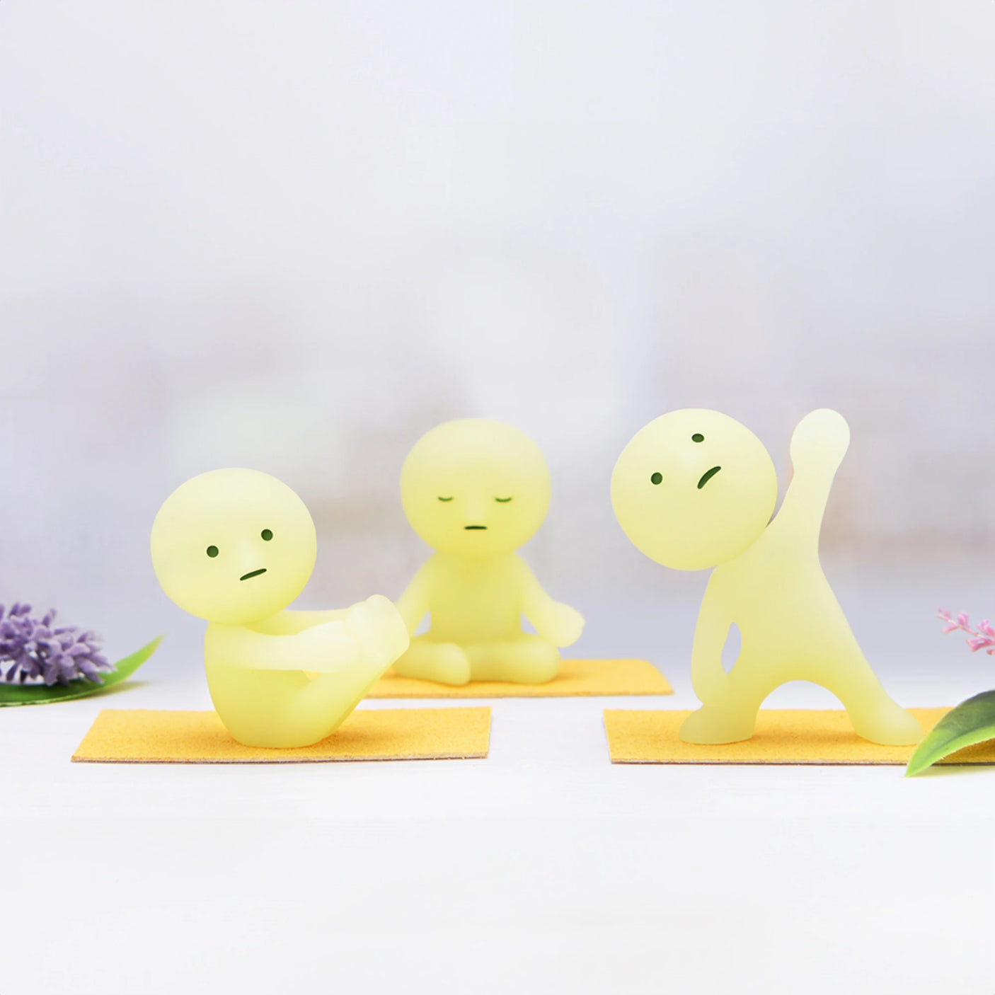 Three small figurines from the Smiski Yoga Series - Blind Box by Smiski are on mats, posed in calming yoga positions. Two of them are sitting, and one stands with an arm raised. These glow-in-the-dark figures add a serene touch to any space.