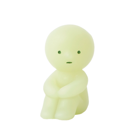 A compact, round-headed figurine in a gentle shade of green sits with its arms resting on its knees and showcases minimal facial features. This Smiski ZipperBite - Hugging Knees from the Smiski brand is a glow-in-the-dark zipper accessory that brings a whimsical charm to your belongings.