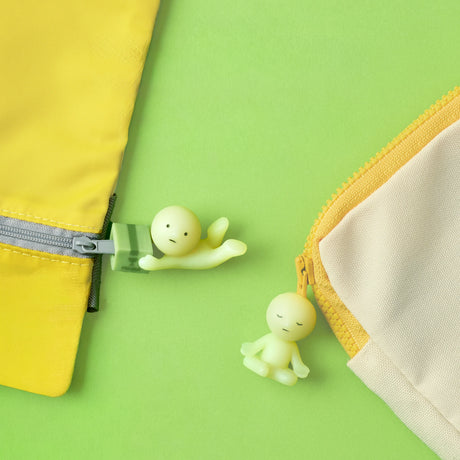 Two pastel pouches with Smiski ZipperBite - Falling Down zipper pulls by Smiski, shaped like small green figures, are displayed on a green background—a cute accessory clip to add charm and fun to your essentials.