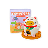 A collectible vinyl figure of a cat with a red collar and kanji symbol rests on a yellow base. Behind it, the box labeled "Smoko Tayto Potato Cat Blind Box" features the playful Tayto Potato.