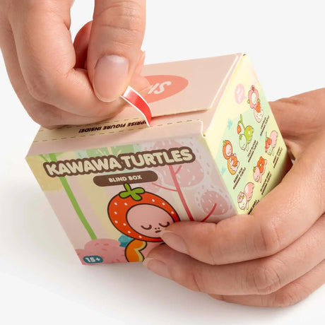Hands peeling open a pastel-colored Smoko Kawawa Turtles blind box with cute turtle illustrations on white background