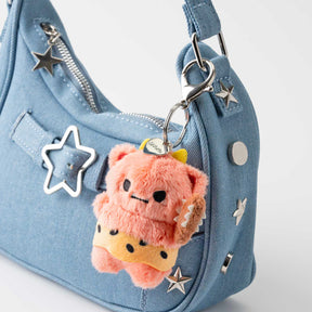 Smoko Roni Oni plush keychain with cheeky grin hanging from blue handbag adorned with silver star studs and zipper pull