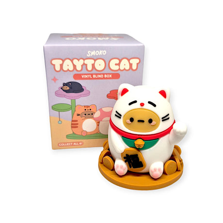 A collectible vinyl toy cat, named Tayto Potato Cat from Smoko, featuring a raised paw and a red collar is elegantly displayed on a pedestal. Behind it, a box labeled "Smoko Tayto Potato Cat Blind Box" highlights an illustration of the delightful feline.