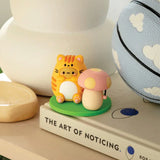 Adorable figurines of an orange tiger and a mushroom are displayed on a table next to a basketball, the Smoko Tayto Potato Cat Blind Box collectible, and a book titled "The Art of Noticing.