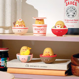 Charming vinyl figures resembling various food items, such as Smoko's Tayto Potato Ramen character, are displayed in small bowls on shelves alongside bottles and a journal, adding a playful touch to the collection.