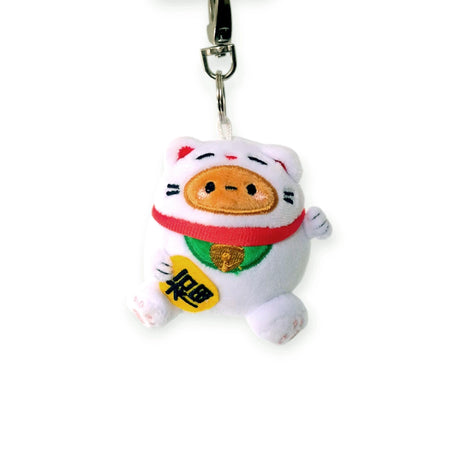 The Smoko Tayto Potato Lucky Cat Keychain Plushie showcases a white cat with an orange nose and pink ears, complemented by a red collar and green bib. Its charm is enhanced by holding a yellow plaque with black symbols, making it an ideal lucky charm for your everyday adventures.