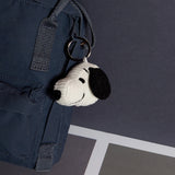 A Snoopy Head Keychain 4.5cm - Corduroy Cream adds a playful touch to a dark blue backpack, setting the stage for Peanuts adventures against a subtle gray backdrop.