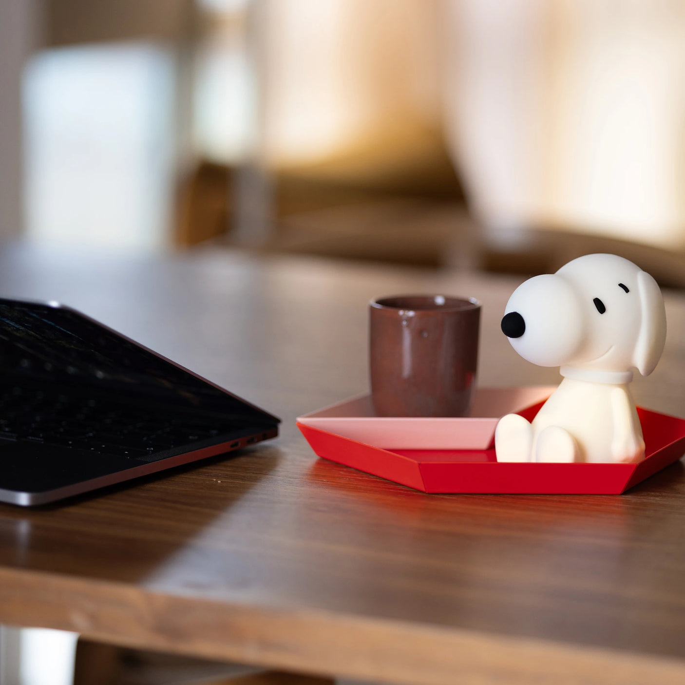 On a table sits a laptop next to a brown mug and red tray holding a small Snoopy Night Light, an 11cm durable and charming BPA-free silicone figurine inspired by the Peanuts character.