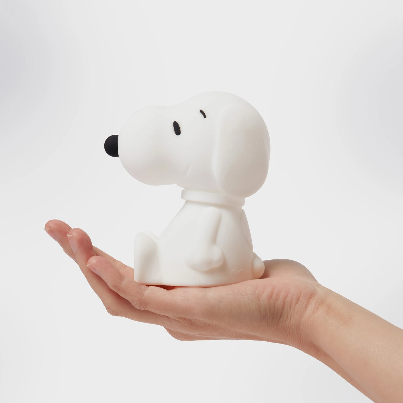 A hand holds a small, white Snoopy figurine against a plain background, reminiscent of the charming 11cm Snoopy Night Light by Snoopy that softly glows with nostalgia.