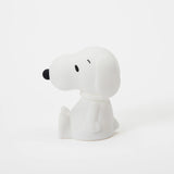 A petite, white Snoopy figure from the Peanuts series, featuring a black nose and closed eyes, is nestled on a simple backdrop. Made from BPA-free silicone, this delightful Snoopy Night Light by the brand Snoopy serves as an ambient 11cm light to softly brighten your surroundings.