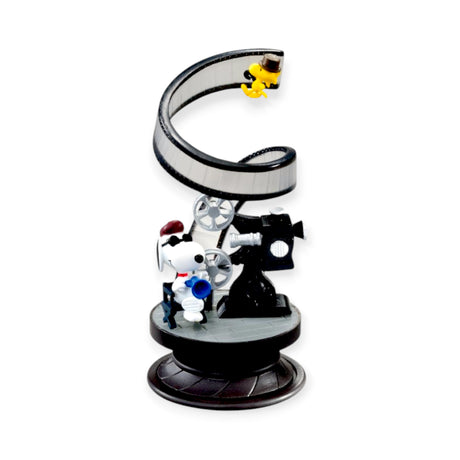 Snoopy dressed as a filmmaker with Woodstock on a spiral film reel atop a black rotating display base