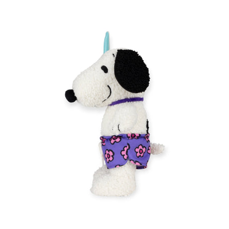 Side profile of Snoopy plush in purple floral swim trunks with blue surfboard on white background