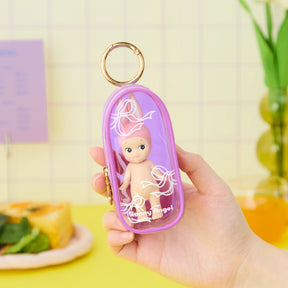 A hand holds the Sonny Angel My Bestie Case - Purple by Sonny Angel, a transparent mini figure carry case with a gold keyring that keeps your doll secure and stylish.