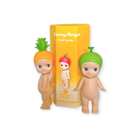 Two small figurines with fruit-themed hats, one styled as a pineapple and the other as a melon, are positioned in front of a yellow box labeled "Sonny Angel Fruit Series Blind Box" from Sonny Angel.