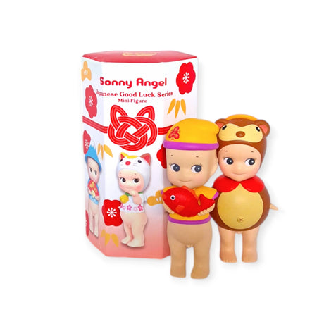 Two mini figures from the Sonny Angel Japanese Good Luck series are displayed in front of a red and white box. One figure wears a yellow hat and holds a fish, while the other is dressed in a bear costume, both acting as delightful lucky charms.