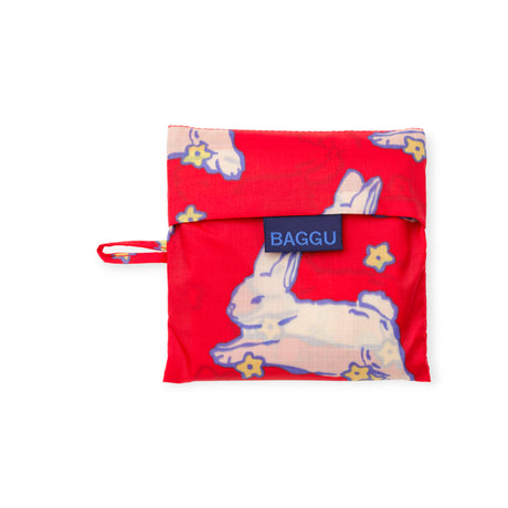 Folded red reusable pouch with white bunny and yellow flower pattern and navy BAGGU label on white background