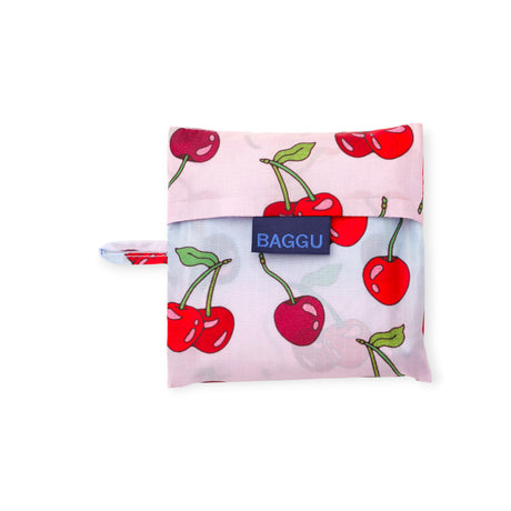 Folded reusable shopping bag with red cherry print on light pink background and blue logo patch