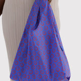 Mini tote bag in cobalt blue with red smiley circle print, held by handles