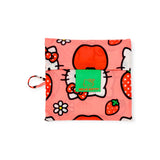 The Baggu Standard Bag - Hello Kitty Apple is a folded pink bag adorned with Hello Kitty, strawberries, flowers, and apples. Made from eco-friendly recycled materials, it features a green label that reads "Hello Kitty.