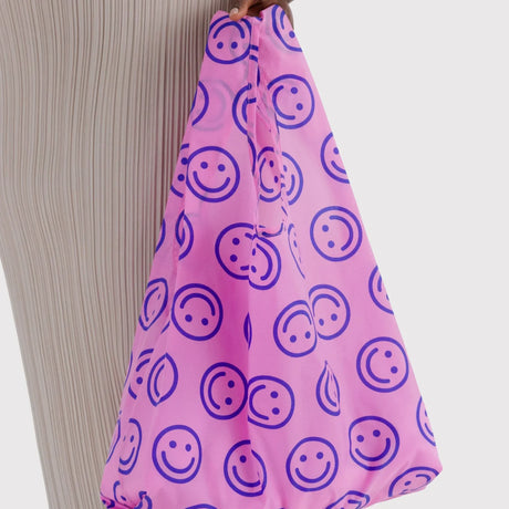 Pink tote bag with navy smiley face print, held by the strap