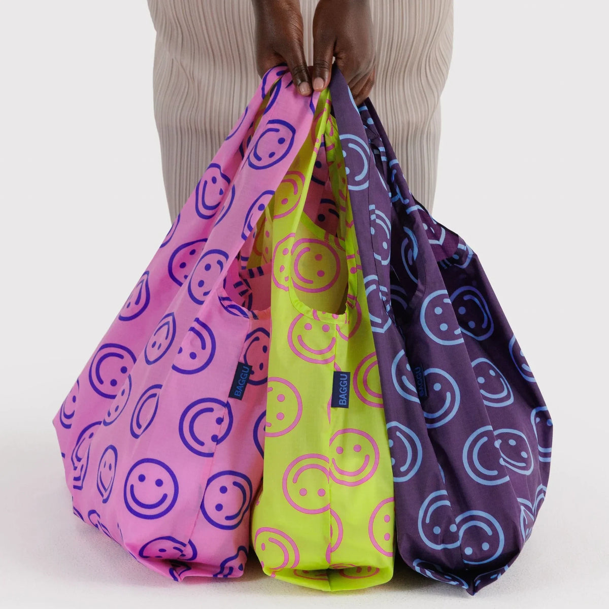 Three bunched drawstring bags with smiley prints, held by their handles.