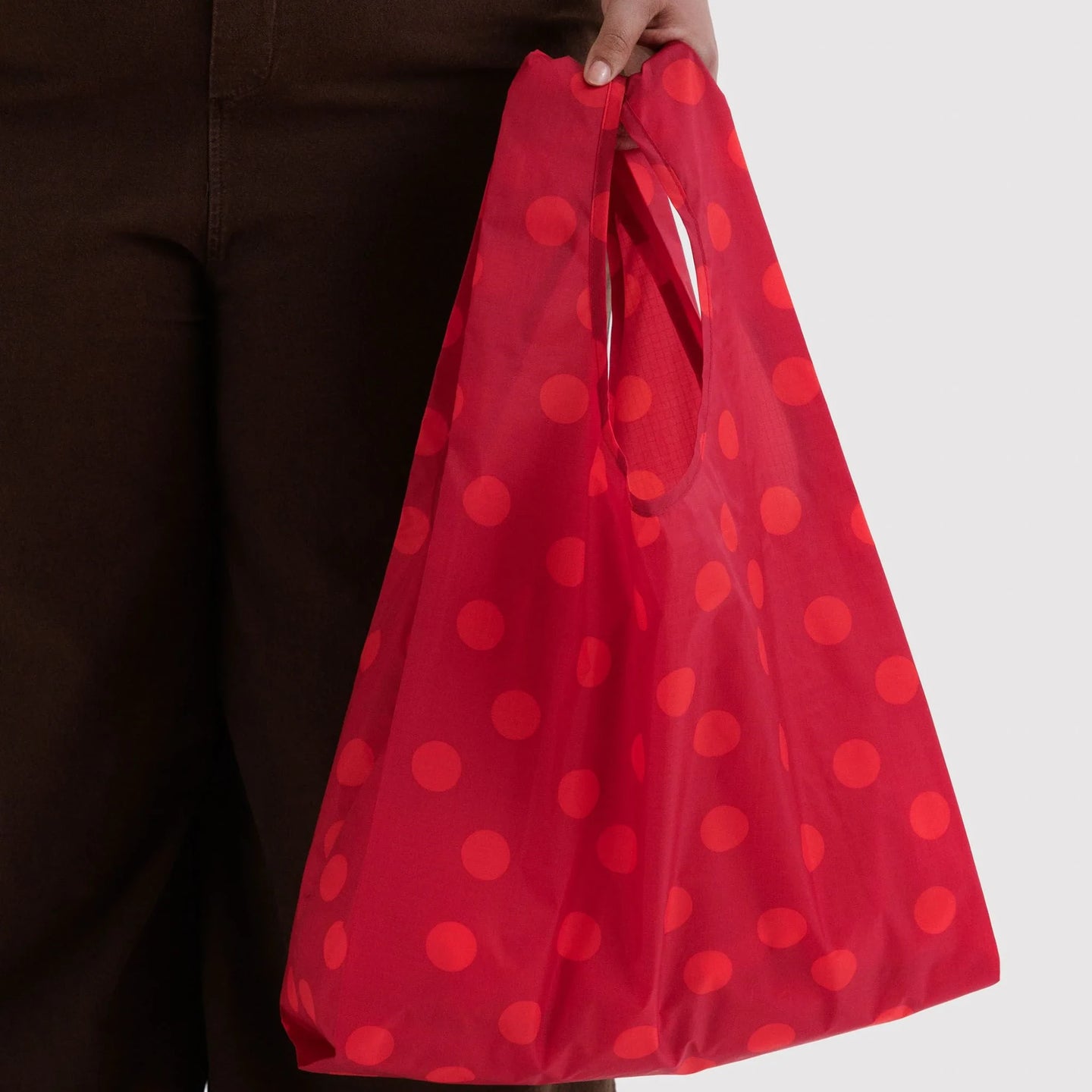 Baggu standard reusable tote bag in red polka dots, carried by hand