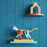 The Wall Art Puzzle - Mochi Cat by Studio Roof features a colorful 3D mochi cat sculpture on a pastel shelf with an orange and beige arch, offering eco-friendly decor for any modern space.
